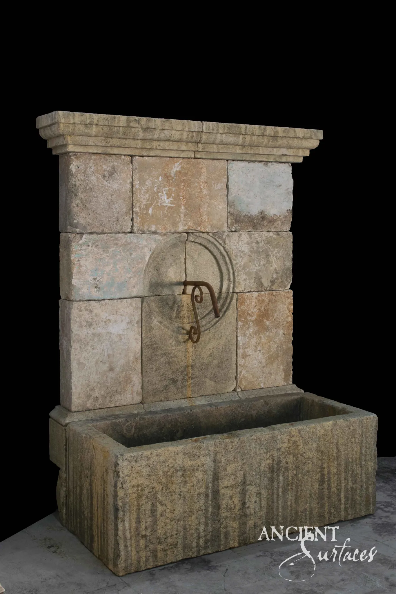Reclaimed antique limestone wall fountain from Ancient Surfaces built in squared blocks with an iron scroll spout above a long stone trough