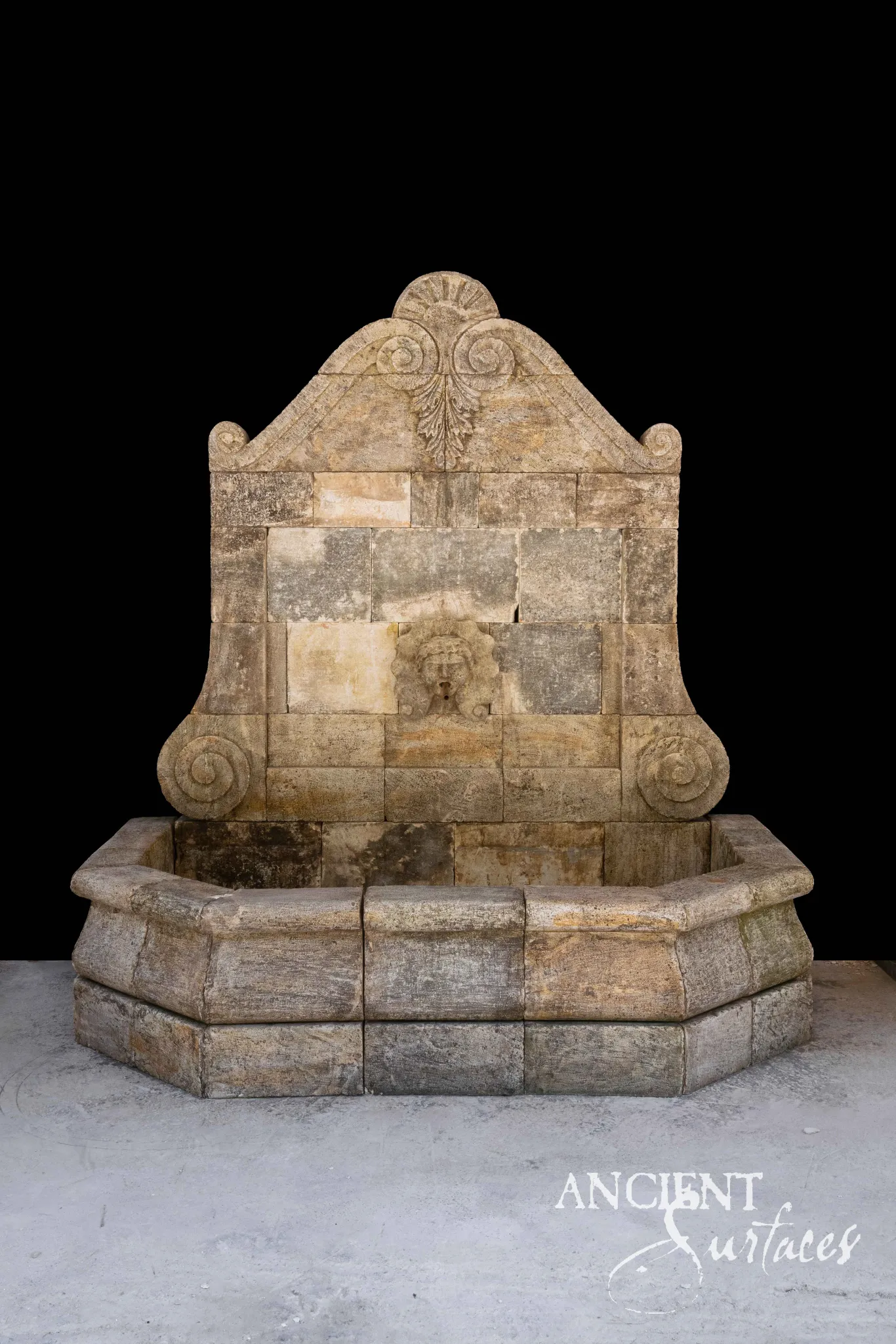 Ancient Surfaces reclaimed antique limestone wall fountain with a scrolled pediment above an octagonal stone basin