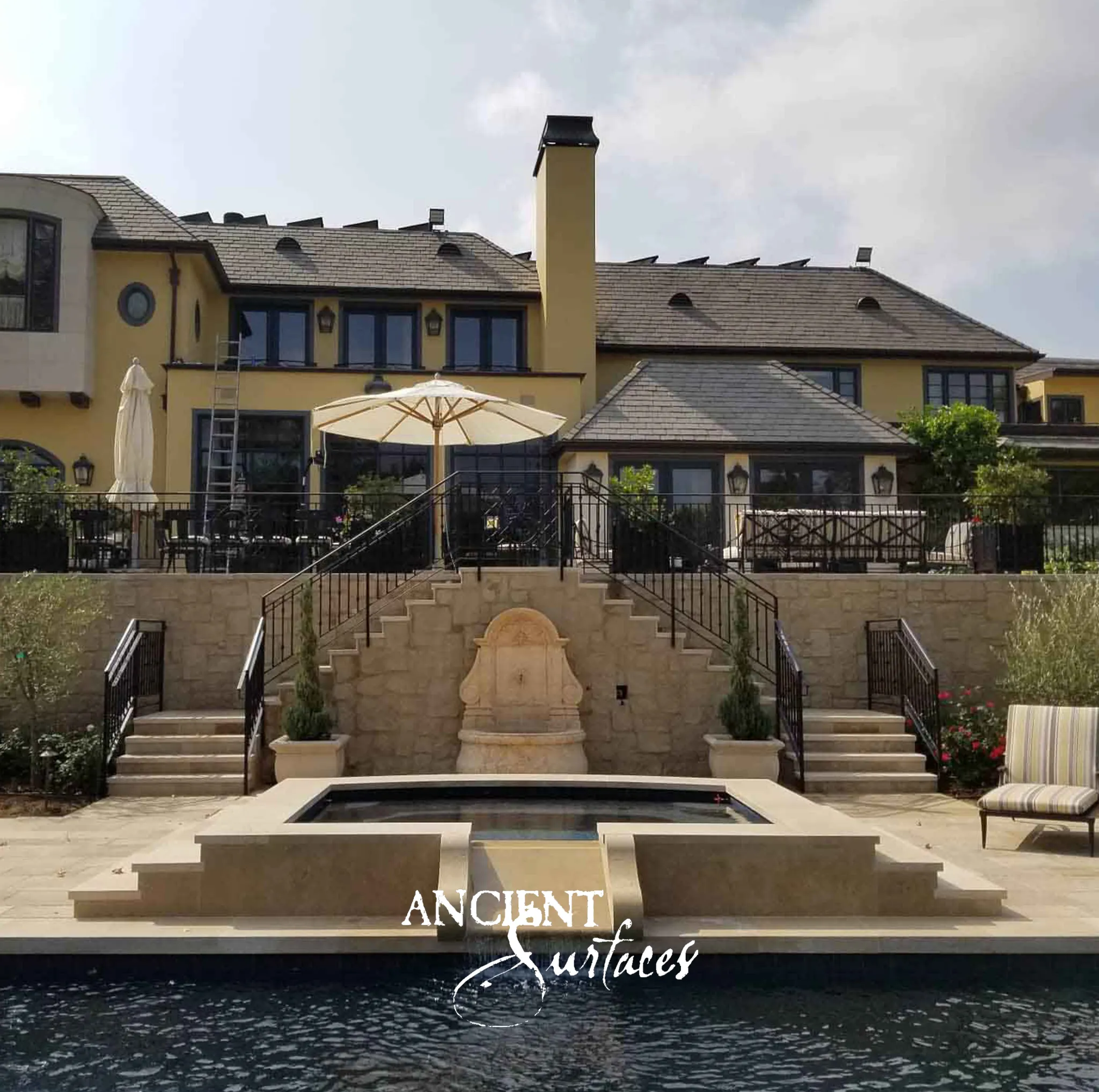Ancient Surfaces reclaimed limestone wall fountain set into a stone terrace wall above a pool between twin staircases