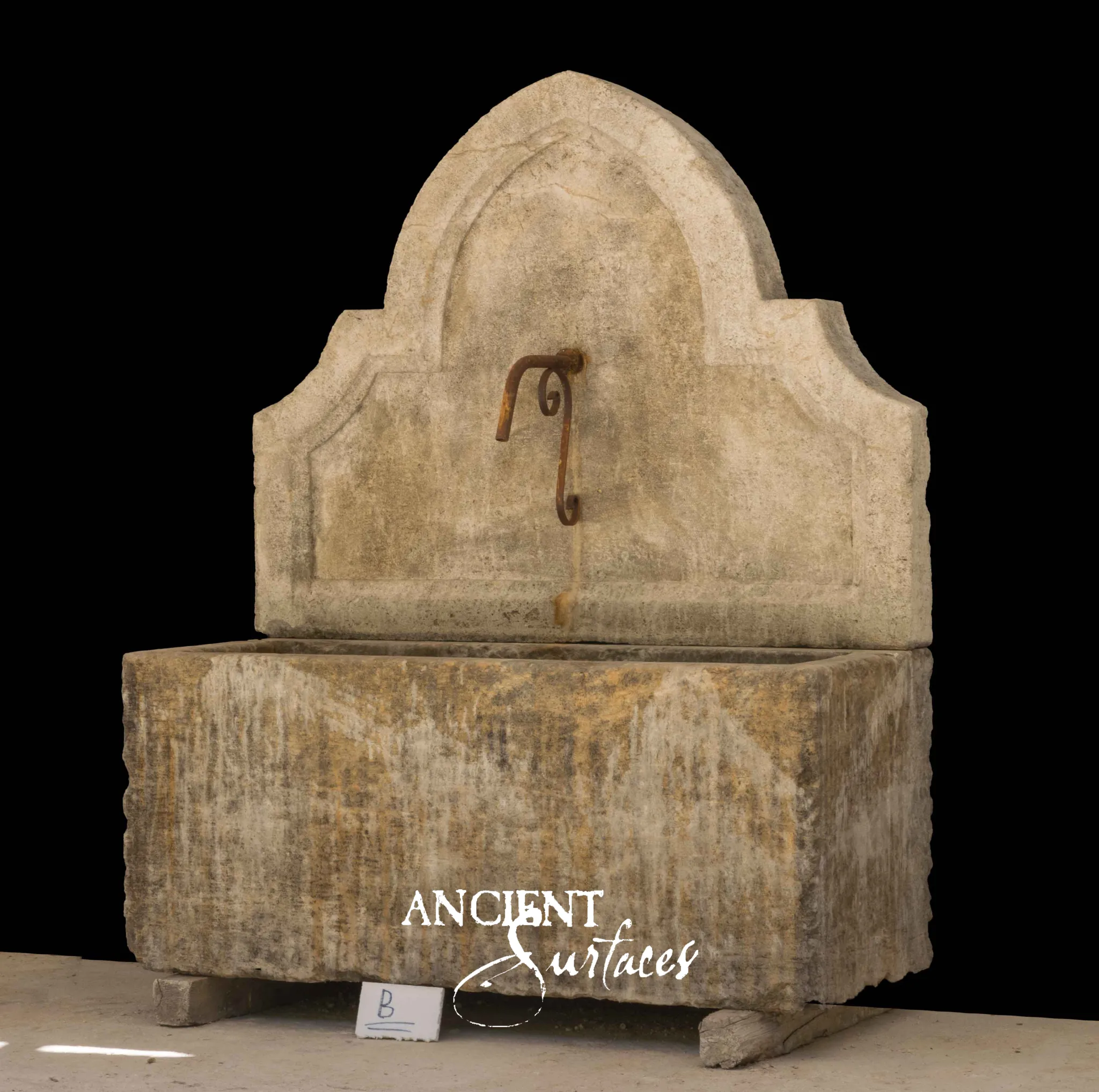 Reclaimed antique limestone wall fountain from Ancient Surfaces with a pointed ogee arch back slab above a monolithic stone trough