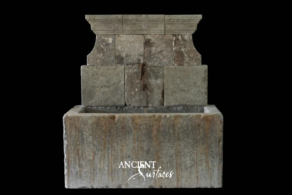 Reclaimed antique limestone wall fountain from Ancient Surfaces built in stepped blocks with a moulded cornice above a long stone trough