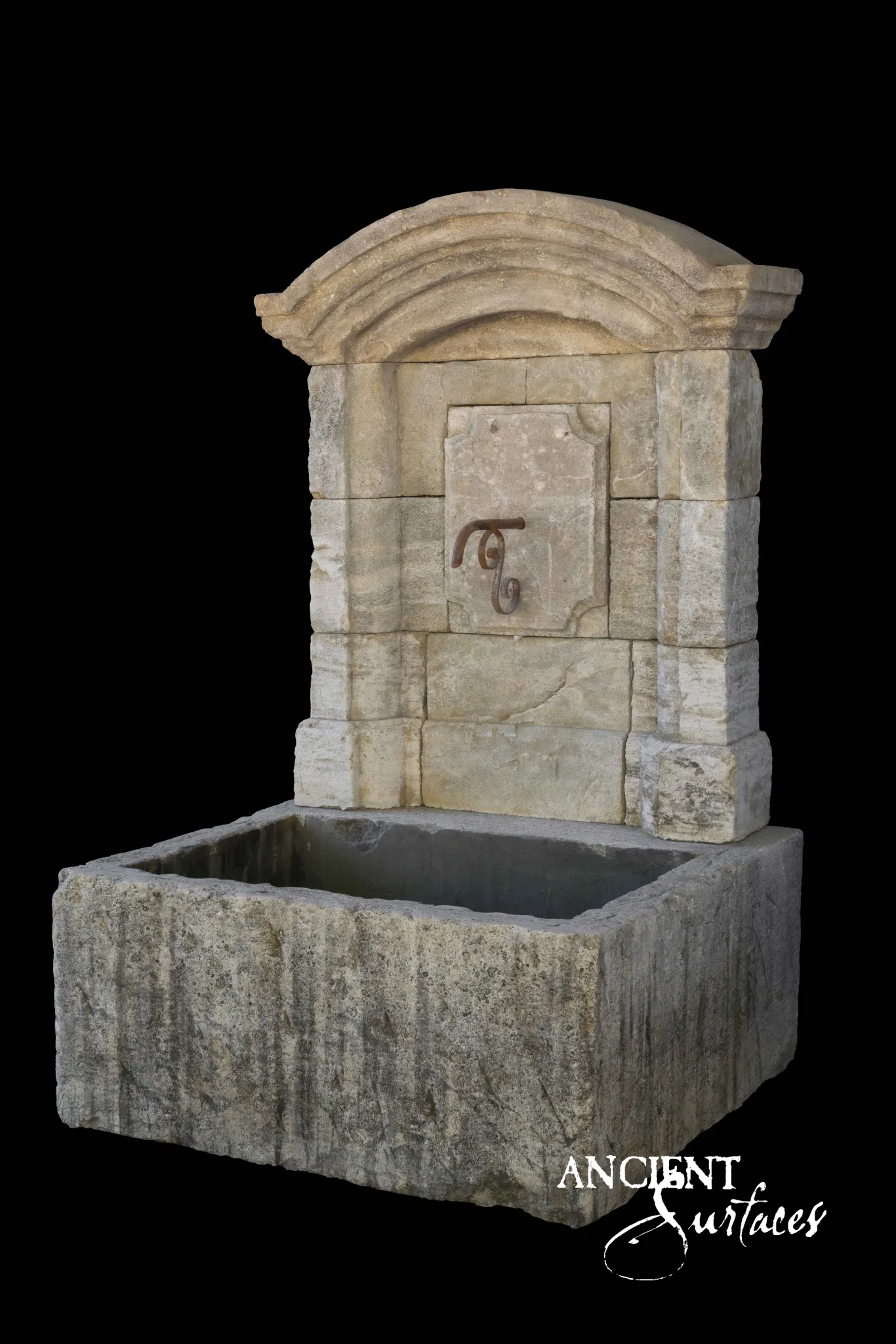 Reclaimed antique limestone wall fountain from Ancient Surfaces with an arched cornice, iron scroll spout and deep stone trough
