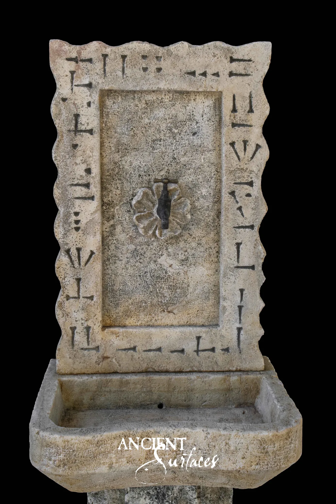Reclaimed antique limestone wall fountain from Ancient Surfaces with a chiselled scalloped frame and bronze rosette tap above a stone basin